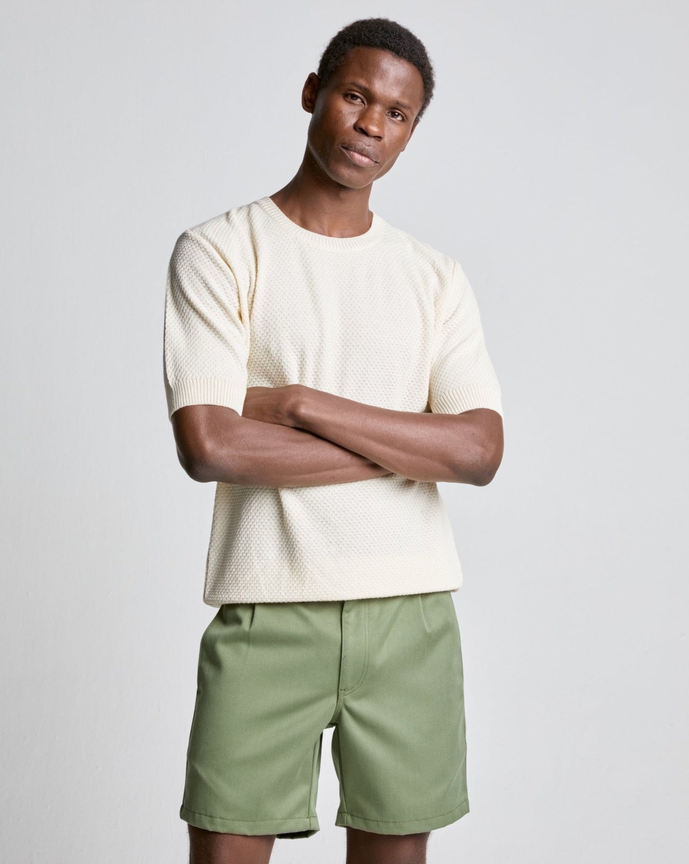 A male model wearing an ecru color waffle knitted tee with short sleeves and green shorts.